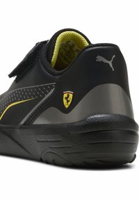 Czarny but sportowy z teksturowaną cholewką z odblaskowym szarym akcentem i żółtym wnętrzem. Posiada logo Ferrari oraz pasek na rzep.