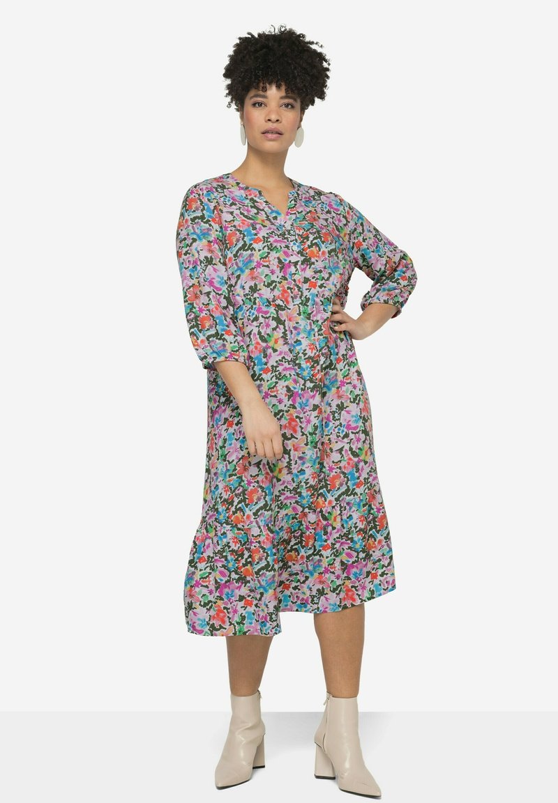 Robe midi florale en tissu léger avec un décolleté en V, des manches trois quarts et un ourlet à volants. Les couleurs incluent le rose, le vert et l'orange.