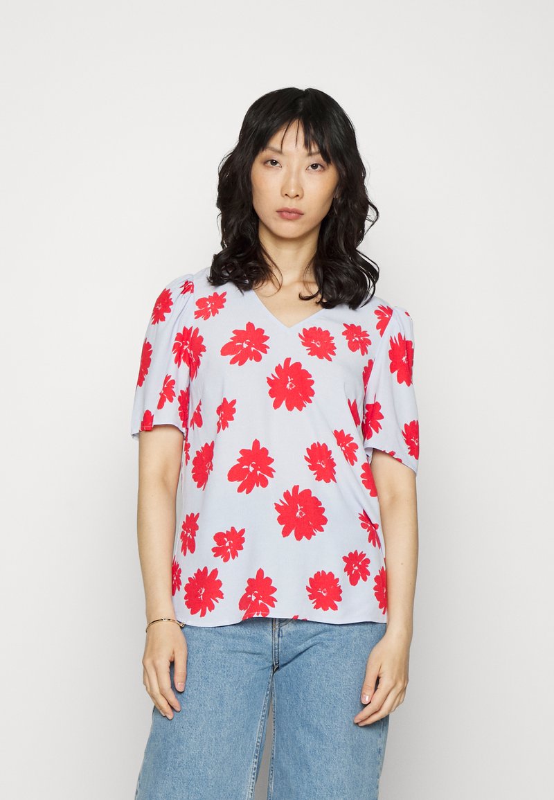 Top floral com decote em V em tecido azul claro, apresentando padrões de flores vermelhas, mangas curtas bufantes e um corte descontraído.