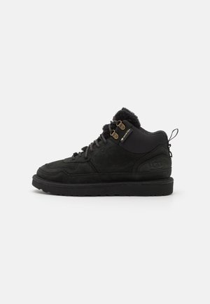 Botte d'hiver noire à mi-hauteur avec doublure en fourrure, lacets à l'avant avec œillets métalliques, semelle épaisse et étiquette Gore-Tex sur le côté pour l'imperméabilité.