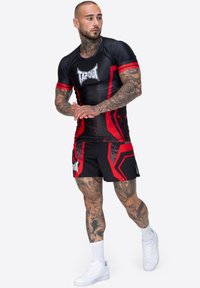 Conjunto atlético negro y rojo con una parte superior ajustada que presenta patrones de salpicadura y un logo, combinado con pantalones cortos que exhiben acentos geométricos.