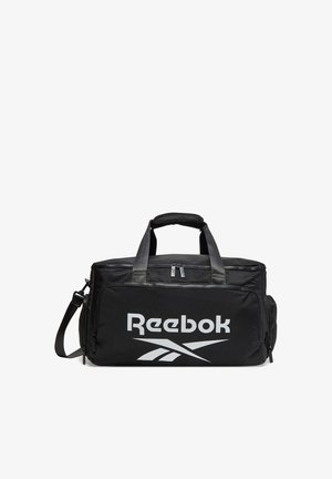 Czarna torba Reebok typu duffel z podwójnymi uchwytami, odpinanym paskiem na ramię, przednią kieszenią na zamek i dużym białym logo.