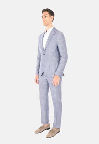 Completo a righe blu chiaro realizzato in tessuto con una finitura texurizzata, caratterizzato da un blazer a un bottone e pantaloni su misura, abbinato a scarpe beige.