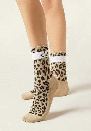 Legs wearing beige socks with black and brown leopard spots and a white ribbed cuff featuring black text "clz" on a plain background.