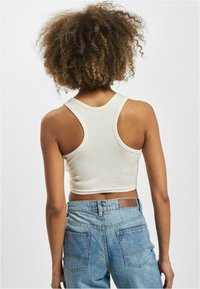 Witte geribbelde crop top met brede armsgaten en ronde halslijn, gecombineerd met high-waisted vervaagde blauwe jeans. Effen stof, geen zichtbare patronen.