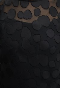 Μαύρο ύφασμα με διαφανή επάνω περιοχή και ανυψωμένα υφασμάτινα ακανόνιστα οβάλ μοτίβα που καλύπτουν την επιφάνεια.