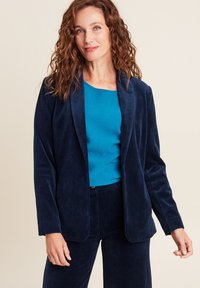 Blazer in corduroy blu navy con rever a lancia, abbinato a un top teal. Il blazer presenta una consistenza morbida e una vestibilità rilassata.