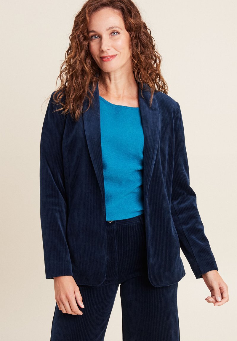 Blazer in corduroy blu navy con rever a lancia, abbinato a un top teal. Il blazer presenta una consistenza morbida e una vestibilità rilassata.