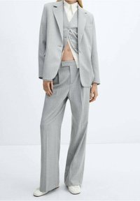 Harmaa pinstripe-puku, jossa on leveät lahkeet, yksirivinen bleiseri ja yhteensopiva liivi. Sujuva kangas hienovaraisella tekstuurilla.