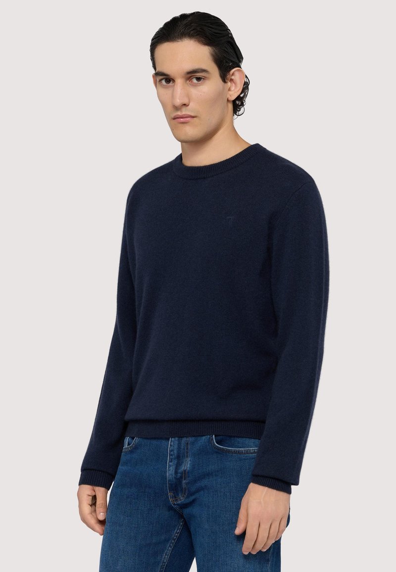 Mörkblå stickad tröja med rund halsringning, långa ärmar och ribbade muddar. Strukturerad tyg med en diskret logodetalj på bröstet.