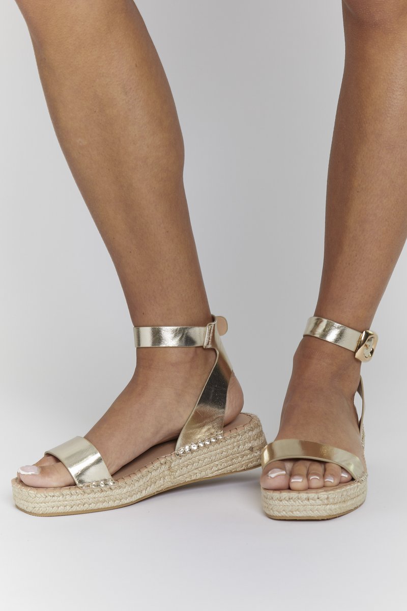 Sandales compensées en métal doré avec semelle en jute tissée. Équipées d'une large sangle et d'une sangle de cheville avec boucle. Texture lisse, design ouvert.