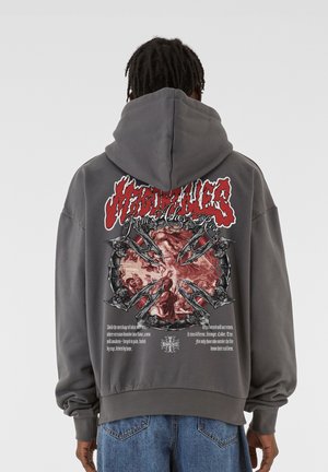 Szara, oversize'owa bluza z kapturem z nadrukiem graficznym na plecach z czerwonymi i czarnymi akcentami oraz napisem. Miękki materiał o lekko teksturowanym wykończeniu.