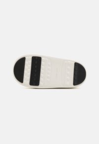 Suola di sneaker bianca con un design testurizzato e sezioni in gomma nera, con motivi circolari e scanalati per garantire aderenza. Forma piatta e arrotondata.
