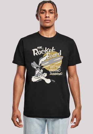 Černé tričko s krátkým rukávem, které zobrazuje kreslenou grafiku postavy s textem "ACME Rocket Board" v bílých a zlatých písmenech.