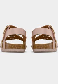 Ροζ σανδάλια με λουριά που διασταυρώνονται, πάτο από φελλό και υφασμένο καουτσούκ πέλμα. Διαθέτουν μεταλλικά στοιχεία με αγκράφα. Εμφανίζεται η πίσω όψη.