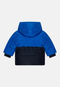 Veste rembourrée présentant un haut bleu vif et un bas navy, avec une capuche, des poignets élastiques et une texture lisse.