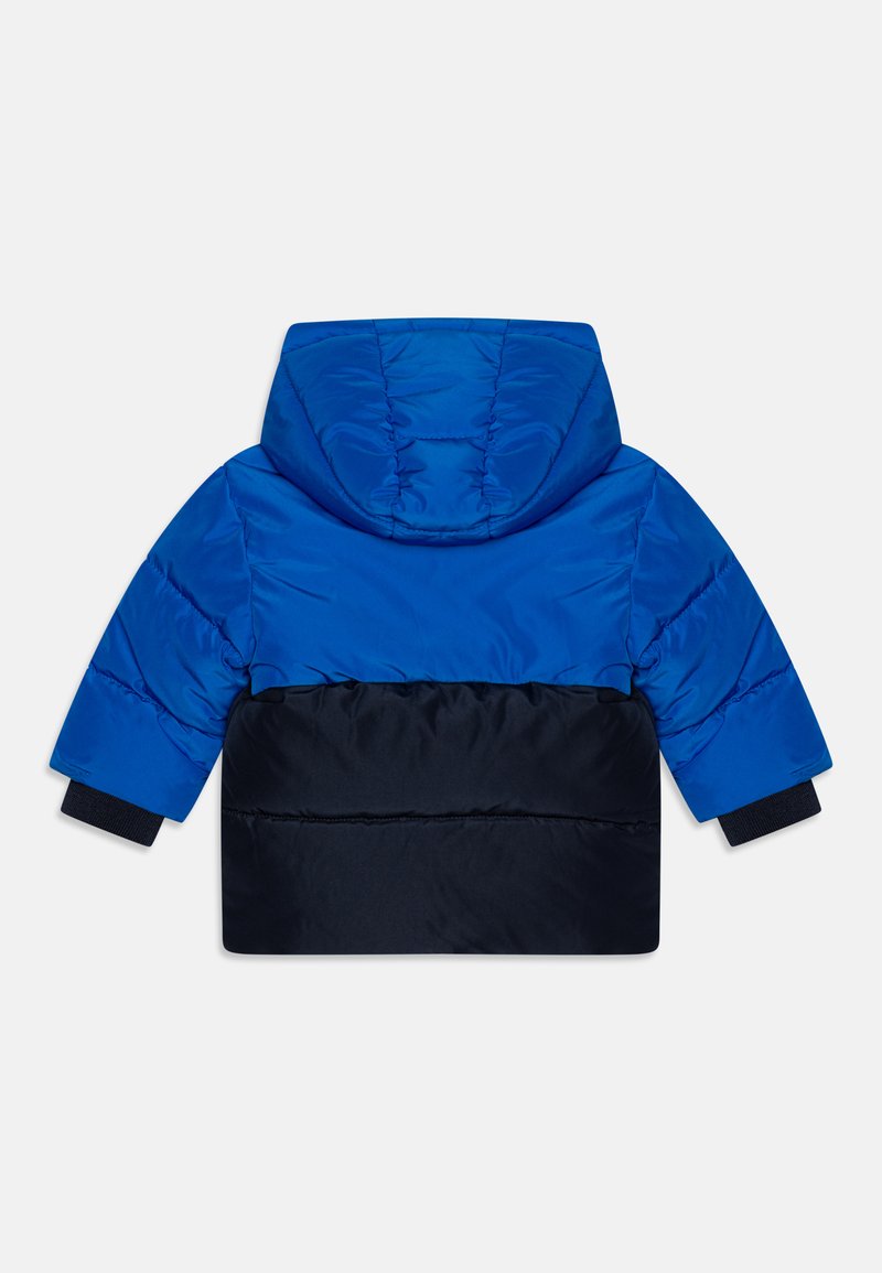 Veste rembourrée présentant un haut bleu vif et un bas navy, avec une capuche, des poignets élastiques et une texture lisse.