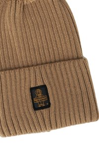 Bruine gebreide beanie met een geribbelde textuur en een omgeslagen rand. Heeft een zwarte patch met een hondenafbeelding en logo in het geel.