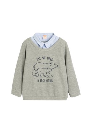Grå sweatshirt med lange ærmer, der har en lyseblå faux-krave skjorte under og et bjørne grafik med teksten "Alt vi behøver er hinanden."