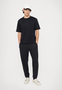 Czarny t-shirt z krótkim rękawem o luźnym kroju, w zestawie z czarnymi spodniami o swobodnym fasonie. Do tego biała czapka i jasne trampki.