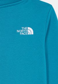 Maglietta a maniche lunghe color turchese realizzata in tessuto morbido, con un logo ricamato bianco de "The North Face" sulla parte sinistra del petto.