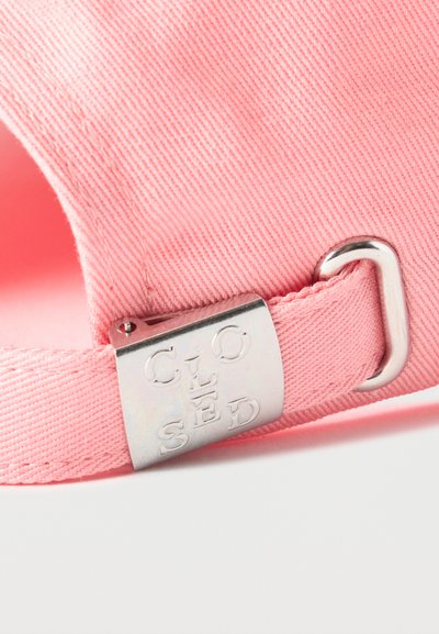 Sangle en tissu rose avec boucle métallique argentée gravée de « CLOSED », attachée à un vêtement ou accessoire rose.