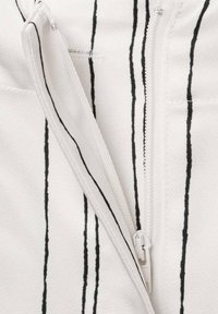 Witte stof met verticale zwarte strepen heeft een ritsdetail, toont een gladde textuur en strakke lijnen. Accenten omvatten gestikte randen.