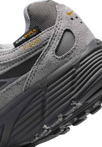 Φτέρνα αθλητικού παπουτσιού σε γκρι και μαύρο χρώμα που δείχνει την υφασμένη σόλα, το σουέτ επάνω μέρος με ετικέτες «CORDURA» και «P-6000» και ένα μικρό κίτρινο λογότυπο Nike.