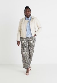 Chaqueta de cuero beige, camisa a rayas azul claro, pantalones de pierna ancha con un patrón de rayas de cebra en negro, beige y crema. Tacones nude con tiras.