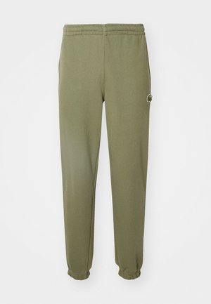 Pantalones de chándal verde oliva hechos de una tela suave, con una cintura y puños elásticos, y un pequeño logo de la marca en el muslo.