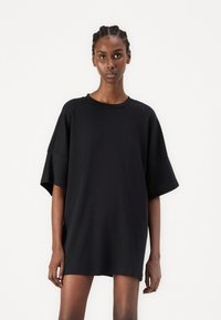 T-shirt negru oversized din bumbac moale, cu guler rotund, mâneci scurte și un croi lejer care se oprește deasupra coapselor.
