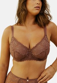 Soutien-gorge en dentelle mauve avec soutien-gorge à armatures, présentant des motifs floraux complexes, des bretelles ajustables et un petit accent doré au centre.
