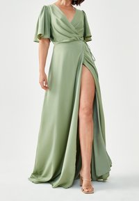 Ljusgrön omlotklänning med korta puffärmar, djup V-ringning och hög slits. Tillverkad av mjukt tyg med en flödande silhuett och knytdetalj.