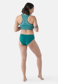 Reggiseno sportivo teal e slip alto abbinati. Il reggiseno presenta un design a schiena scoperta e un materiale testurizzato; gli slip offrono una finitura morbida.