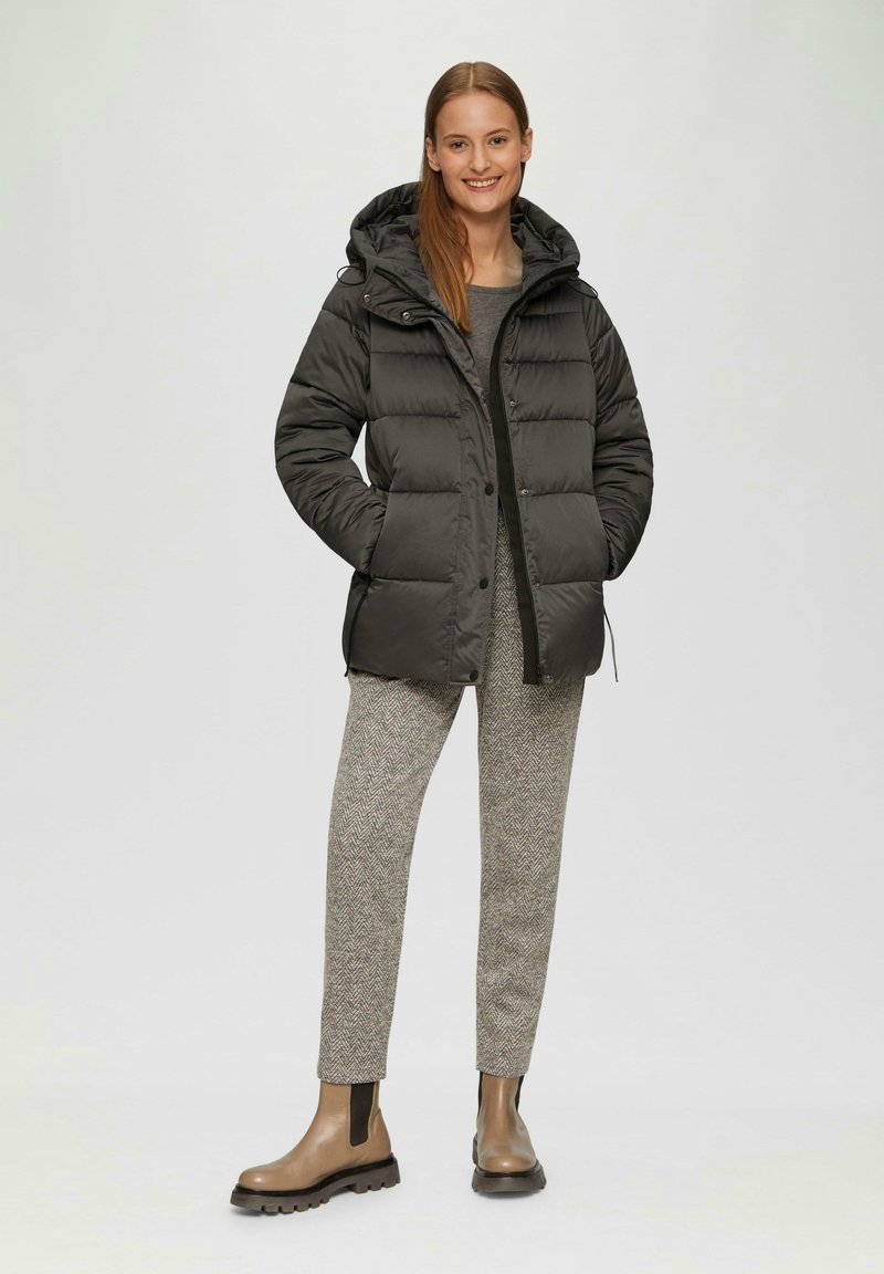 Czarna kurtka puchowa z kapturem, z pikowanym wzorem i zapięciem na zamek. Nosi się ją z wzorzystymi szarymi spodniami i brązowymi botkami za kostkę.