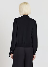 Schwarzer Pullover mit langen Ärmeln, eng anliegenden Bündchen und einem sauberen Saum. Der Stoff wirkt weich, mit glatter Textur und minimalen Details.