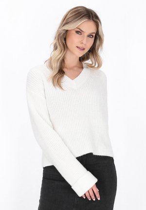 Maglione bianco lavorato a maglia con scollo a V, spalle scese e polsini larghi; abbinato a una gonna di denim scuro. Tessuto liscio, design dalla vestibilità morbida.