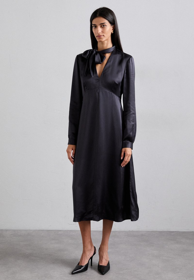 Schwarzes Satin-Midikleid mit langen Ärmeln, tiefem V-Ausschnitt und einer Schleifenakzent am Hals, das ein fließendes Design und eine glatte Textur aufweist.