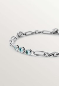 Pulsera de plata que presenta piedras azules circulares unidas por segmentos de cadena alargados, exhibiendo un acabado pulido y una textura suave.