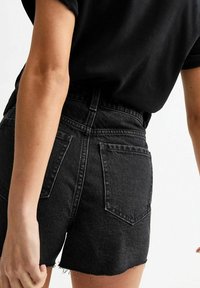 Pantalones cortos de mezclilla negros con dobladillo deshilachado, de tiro alto y dos bolsillos traseros. Presenta un diseño limpio y una tela ligeramente texturizada.