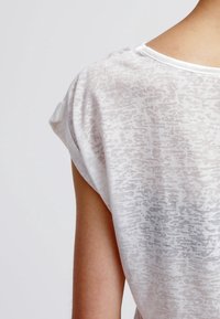 Vit kortärmad topp med en genomskinlig, strukturerad tyg med ett subtilt mönster, rundad halsringning och avslappnad passform.