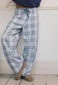 Lysblå og hvide ternede pyjamabukser lavet af blødt stof med elastisk talje og snøre; parret med beige slippers.