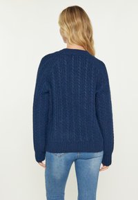 Maglione in blu navy a trecce con orlo a costine e maniche ampie. Il tessuto ha un aspetto strutturato, offrendo calore e comfort.