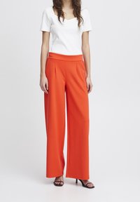 Breda orange byxor med en slät textur och en avsmalnande midja, ihop med en kroppsnära vit topp med fyrkantig halsringning.