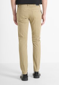 Pantalones beige de corte ajustado, con bolsillos traseros y textura sutil; combinados con zapatos negros. Diseñados con una cintura de media altura.