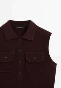 Gilet en maille sans manches marron foncé avec col, fermeture boutonnée à l'avant et deux poches poitrine à boutons.