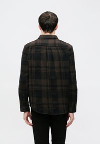 Čierna a hnedá károvaná košeľa, flanelová látka, dlhé rukávy, manžety na gombíky, detail zadného dielu, zakrivený lem. Model zobrazený zozadu.