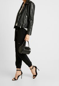 Mustassa nahkasaappaassa on hopeiset vetoketjut, mustat verkkarit ja pyöreä musta käsilaukku. Korkeakorkoiset mustat sandaalit, joissa on nilkkahihnat.