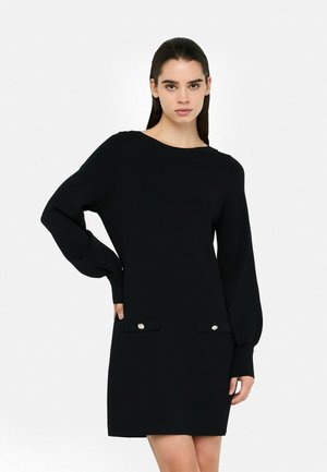 Abito maglione nero con maniche lunghe a sbuffo, scollatura rotonda e due tasche frontali con bottoni dorati decorativi. Texture liscia.