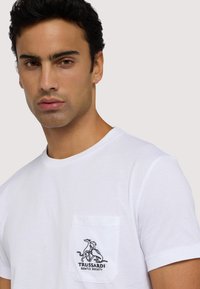 Biała bawełniana koszulka z klasycznym okrągłym dekoltem, z kieszonką na lewej piersi oraz czarnym haftowanym logo z psami i napisem "TRUSSARDI GENTLE SOCIETY."